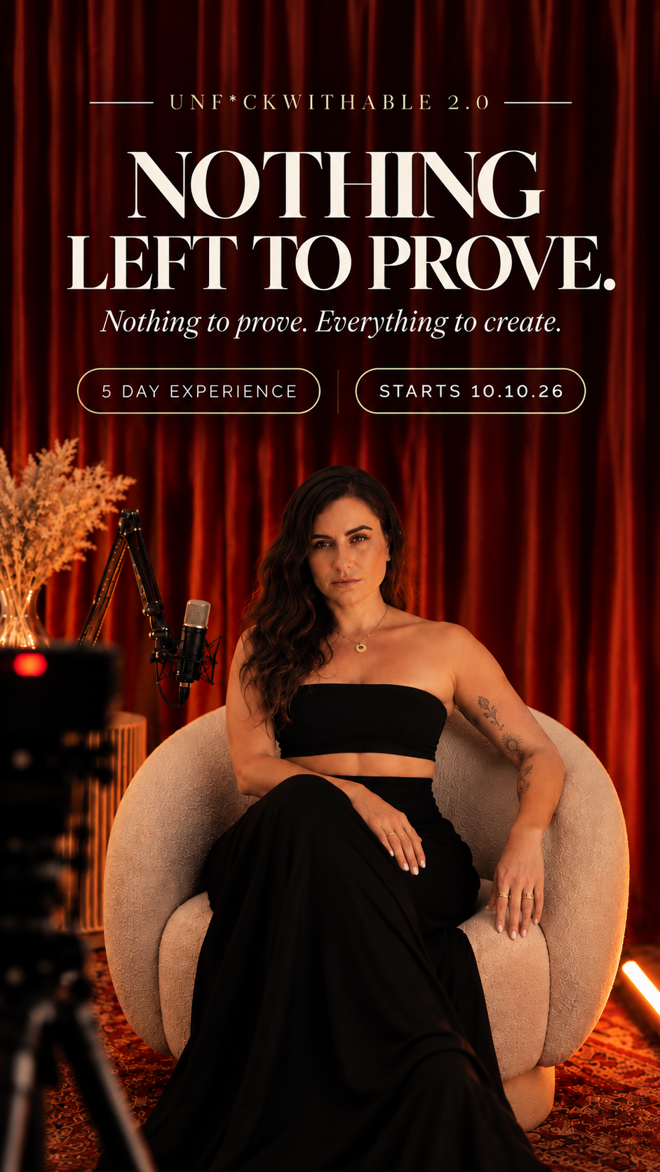 Laura seated in a cream armchair in front of red stage curtains
